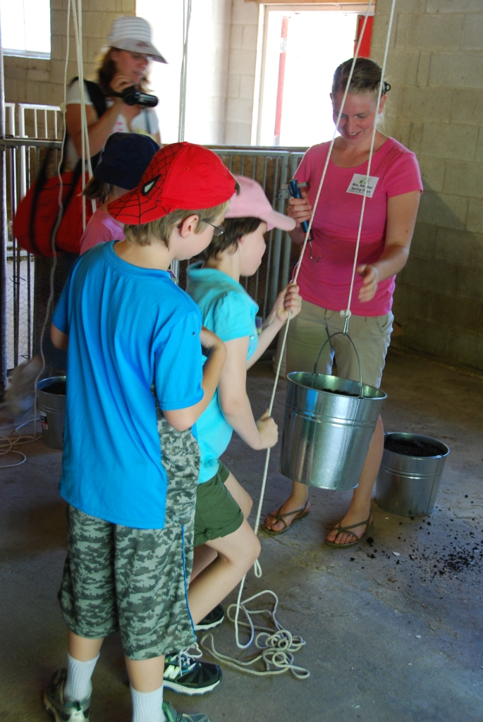 Person showing kids the use of a pulley using a rope and bucket